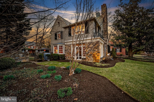 back of property at dusk featuring a lawn, a chimney, stone siding, and stucco siding