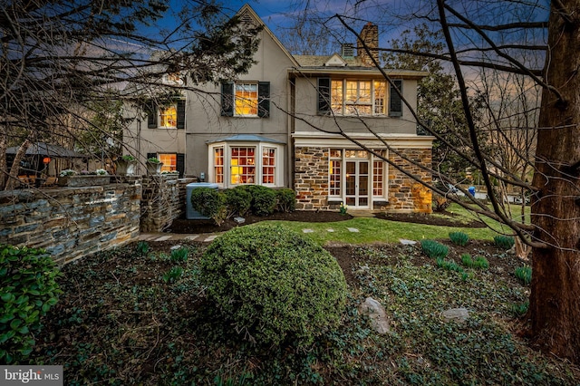 rear view of property featuring stucco siding, stone siding, central AC, and a chimney