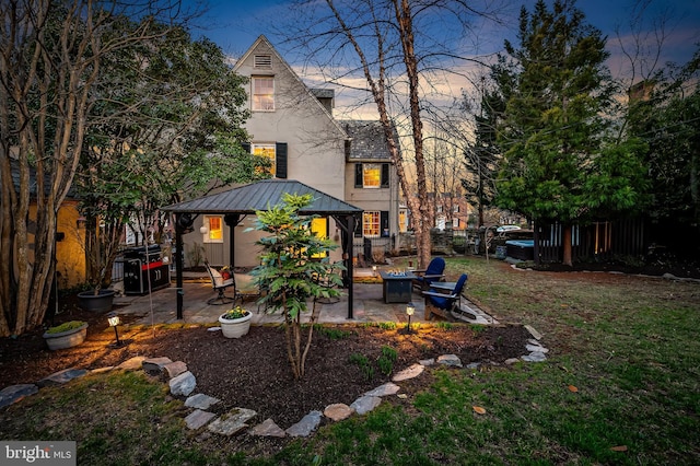back of property at dusk with fence, a yard, stucco siding, a gazebo, and a patio area
