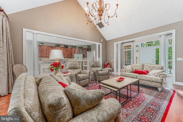 living area featuring visible vents, light wood-type flooring, an inviting chandelier, high vaulted ceiling, and ornate columns