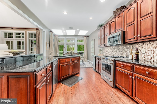 kitchen with backsplash, light wood-style flooring, appliances with stainless steel finishes, a skylight, and a sink