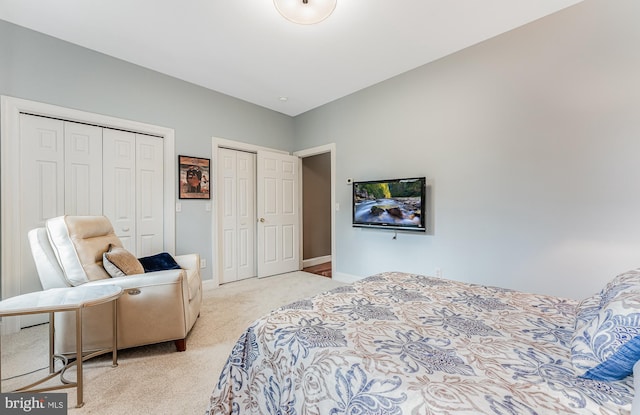 bedroom featuring light colored carpet, two closets, and baseboards