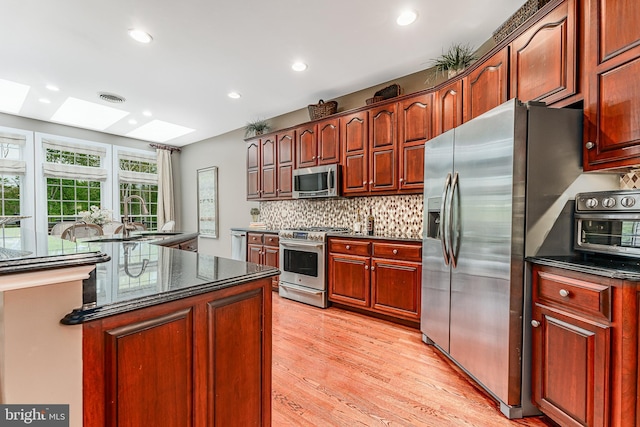 kitchen featuring light wood-type flooring, visible vents, appliances with stainless steel finishes, a skylight, and decorative backsplash