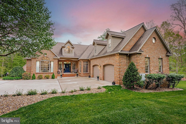 view of front facade featuring a yard, an attached garage, a shingled roof, concrete driveway, and brick siding