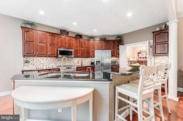 kitchen with light wood finished floors, recessed lighting, decorative backsplash, appliances with stainless steel finishes, and a kitchen breakfast bar