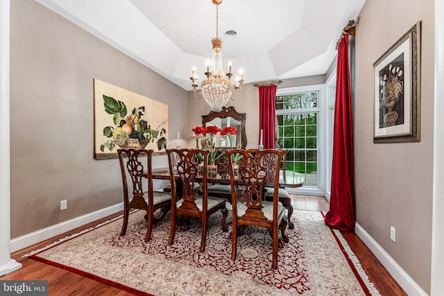 dining room with visible vents, a notable chandelier, a tray ceiling, wood finished floors, and baseboards