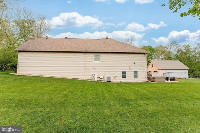 back of property with central AC unit, a hot tub, and a yard