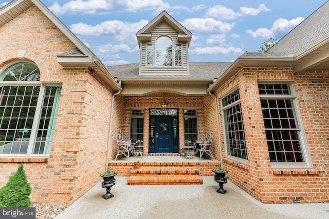 view of exterior entry featuring covered porch, brick siding, and a shingled roof