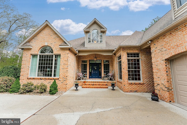 property entrance featuring brick siding, covered porch, and a shingled roof