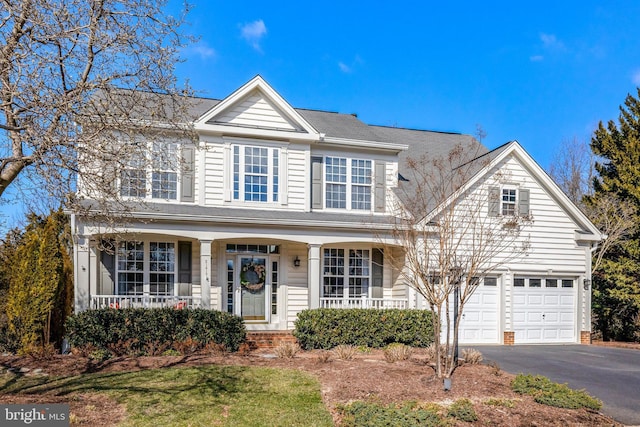 traditional-style house with aphalt driveway, covered porch, and an attached garage