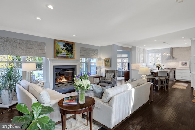 living area featuring dark wood-style floors, recessed lighting, ornamental molding, and a glass covered fireplace