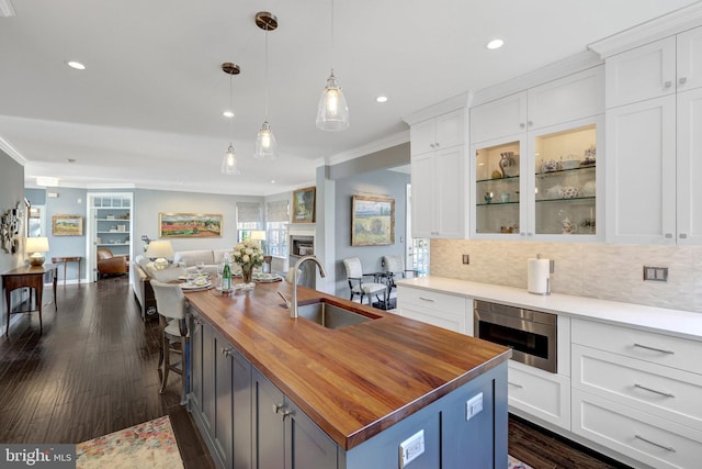 kitchen featuring a fireplace, butcher block counters, open floor plan, white cabinets, and a sink