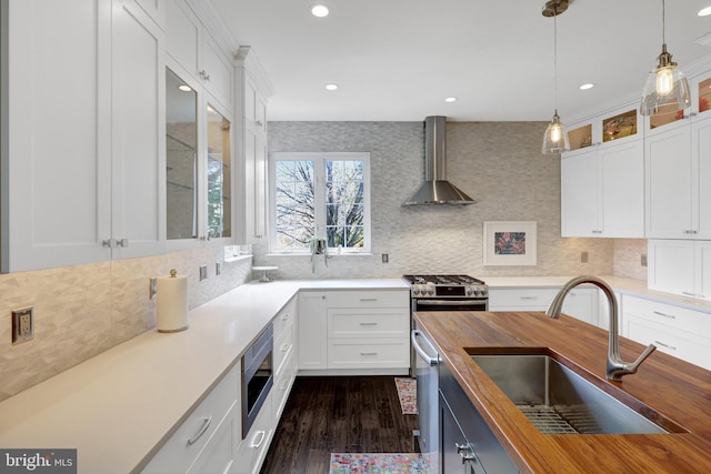 kitchen with a sink, wooden counters, wall chimney range hood, appliances with stainless steel finishes, and decorative light fixtures