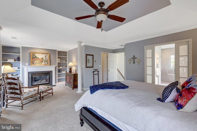 carpeted bedroom featuring decorative columns, a raised ceiling, a glass covered fireplace, ceiling fan, and baseboards