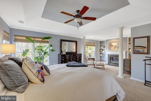 carpeted bedroom featuring visible vents, a tray ceiling, a glass covered fireplace, decorative columns, and crown molding