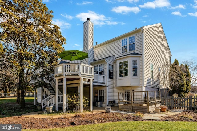 rear view of house with stairs, a deck, a chimney, and fence