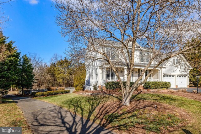 view of front facade with covered porch, an attached garage, fence, driveway, and a front lawn