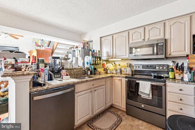 kitchen featuring appliances with stainless steel finishes, light brown cabinets, a sink, and a textured ceiling