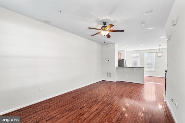 unfurnished living room with dark wood-style floors, baseboards, visible vents, and a ceiling fan