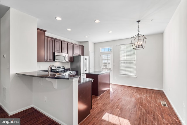 kitchen with appliances with stainless steel finishes, a center island, visible vents, and wood finished floors