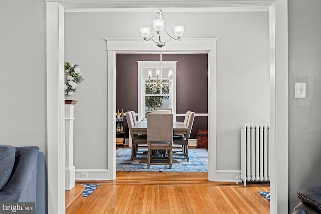 dining space featuring wood-type flooring, baseboards, radiator, an inviting chandelier, and crown molding