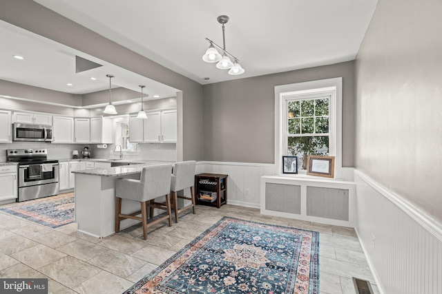 kitchen with visible vents, wainscoting, a breakfast bar area, stainless steel appliances, and white cabinetry