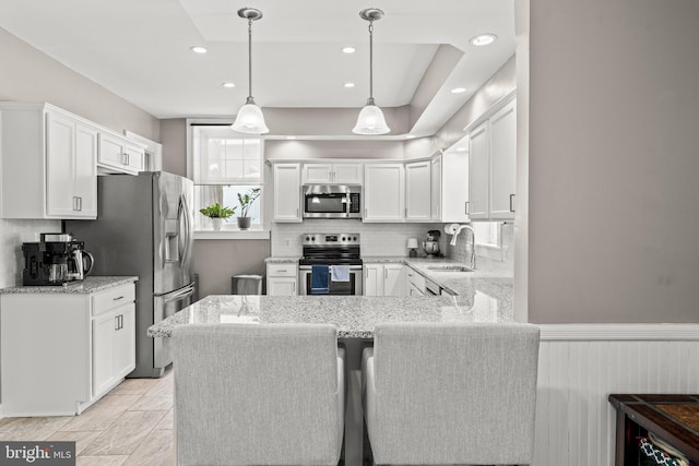 kitchen featuring wainscoting, appliances with stainless steel finishes, a peninsula, white cabinetry, and a sink