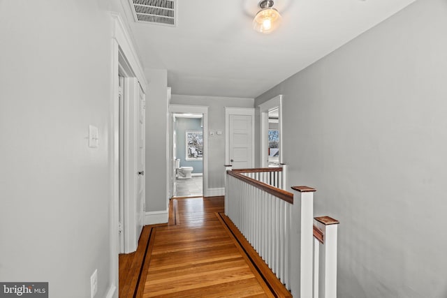 corridor featuring visible vents, wood finished floors, an upstairs landing, and baseboards