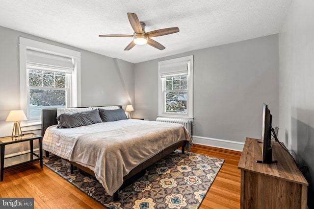 bedroom with light wood-style floors, radiator, multiple windows, and baseboards