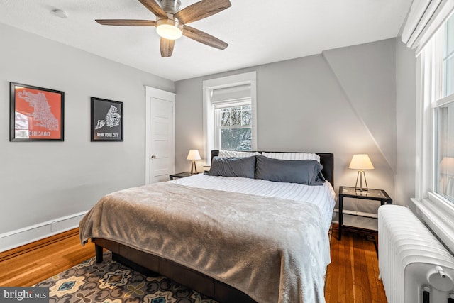 bedroom featuring a ceiling fan, radiator heating unit, baseboards, and wood finished floors