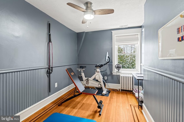 workout area with radiator, wood-type flooring, visible vents, and wainscoting