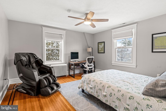 bedroom with multiple windows, radiator heating unit, and hardwood / wood-style flooring