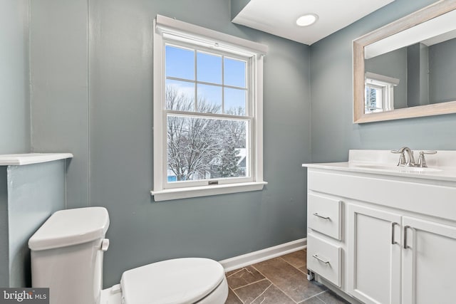 bathroom featuring toilet, a healthy amount of sunlight, baseboards, and vanity