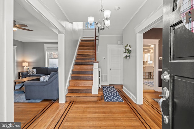 foyer entrance featuring light wood-style flooring, stairs, crown molding, and ceiling fan with notable chandelier