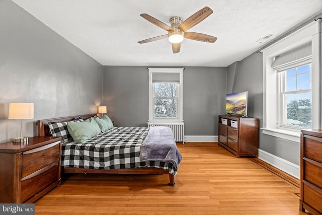 bedroom with light wood-type flooring, radiator, multiple windows, and baseboards