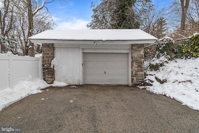 snow covered garage with driveway and fence