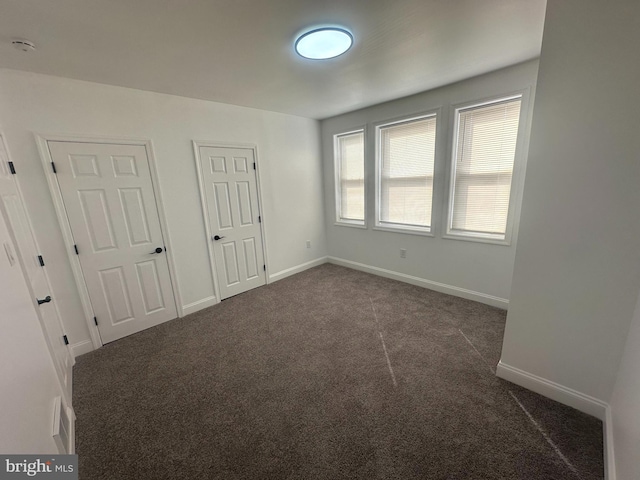 unfurnished bedroom with dark carpet, visible vents, and baseboards