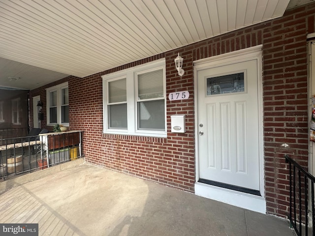 entrance to property featuring a porch and brick siding