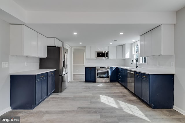 kitchen featuring light wood finished floors, decorative backsplash, appliances with stainless steel finishes, blue cabinetry, and a sink