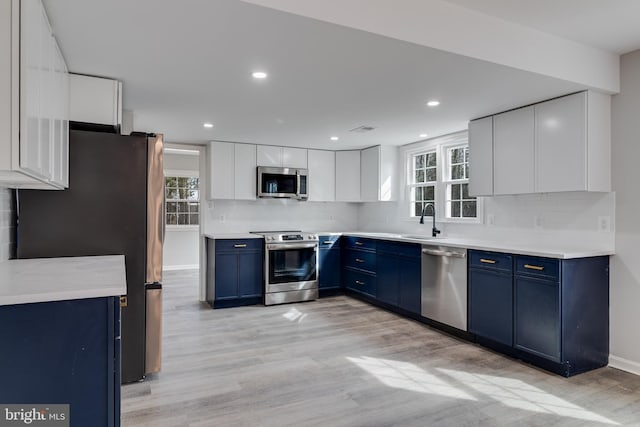 kitchen with blue cabinets, a sink, appliances with stainless steel finishes, decorative backsplash, and light wood finished floors