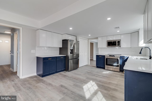 kitchen featuring visible vents, a sink, stainless steel appliances, blue cabinetry, and backsplash