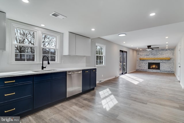 kitchen featuring blue cabinetry, light wood finished floors, a brick fireplace, a sink, and dishwasher