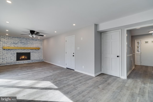 unfurnished living room with a brick fireplace, a ceiling fan, wood finished floors, and recessed lighting