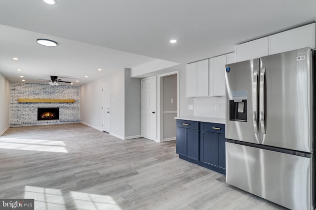 kitchen featuring a ceiling fan, white cabinets, a brick fireplace, stainless steel refrigerator with ice dispenser, and light wood finished floors