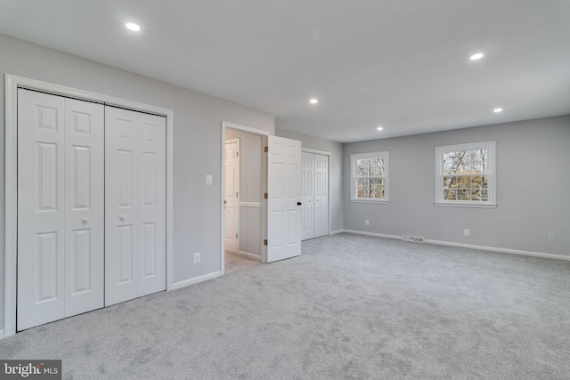 unfurnished bedroom featuring carpet floors, visible vents, two closets, and recessed lighting