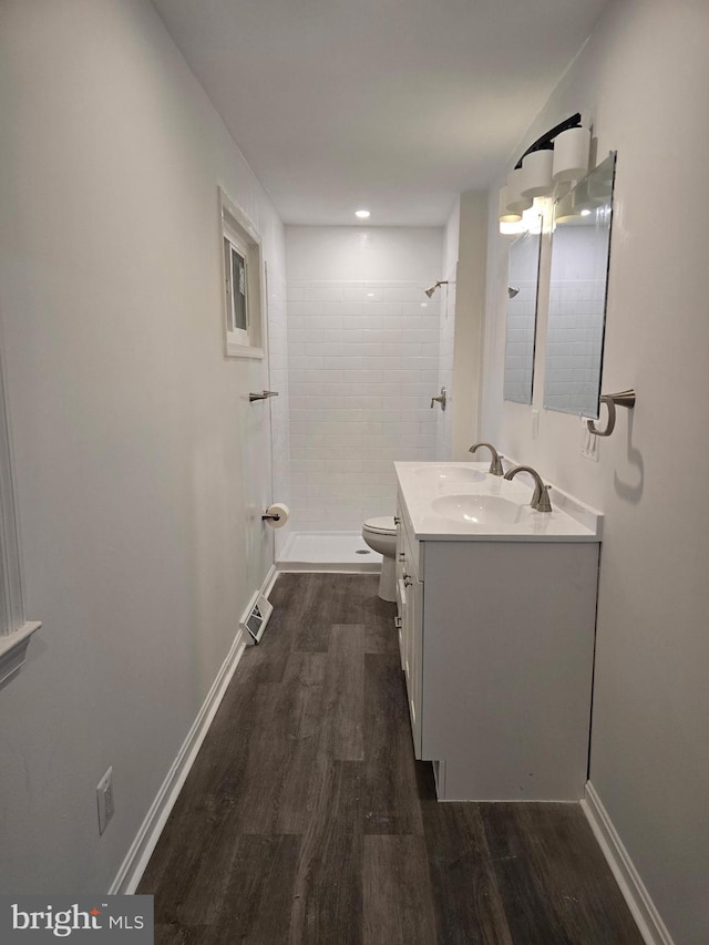 bathroom with a tile shower, vanity, toilet, and wood finished floors