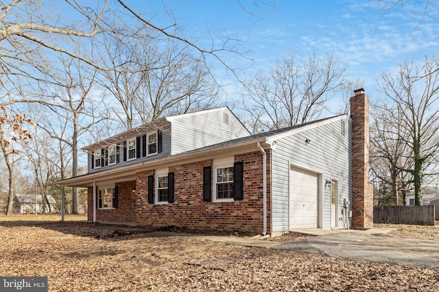 view of side of property with brick siding, a chimney, an attached garage, fence, and driveway