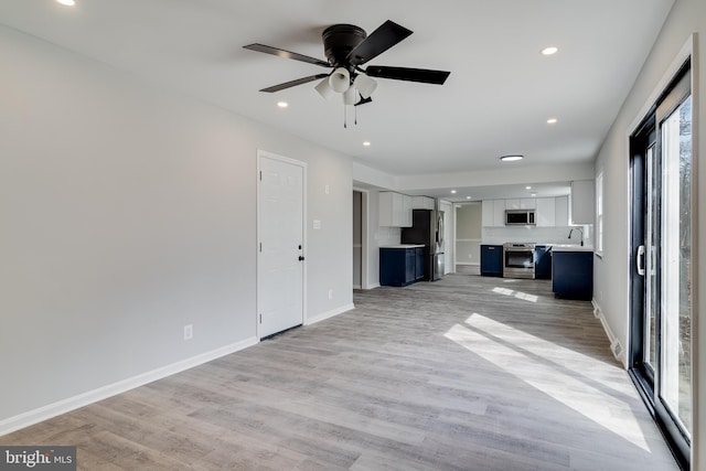 unfurnished living room featuring recessed lighting, a sink, light wood-style flooring, and baseboards