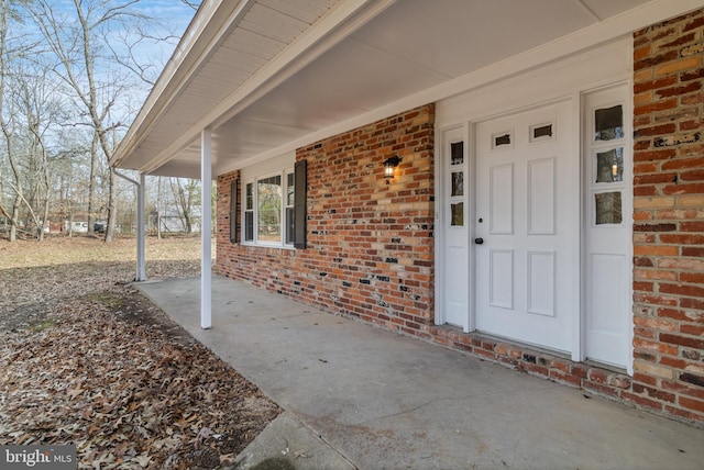 doorway to property with a porch and brick siding