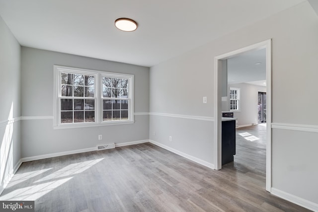 empty room featuring wood finished floors, visible vents, and baseboards